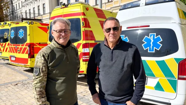 Two men stand in front of yellow and white ambulances delivered through UkraineAid for hospitals and emergency medical support in Ukraine.