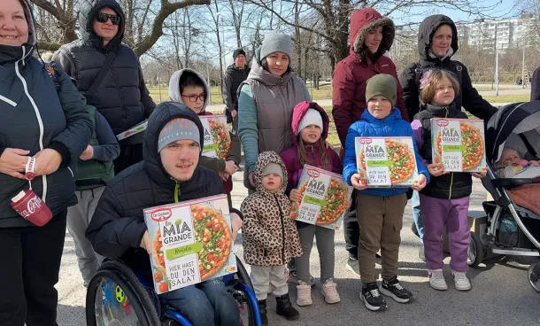 Families with children in Ukraine receive donated pizza boxes during an outdoor food distribution.